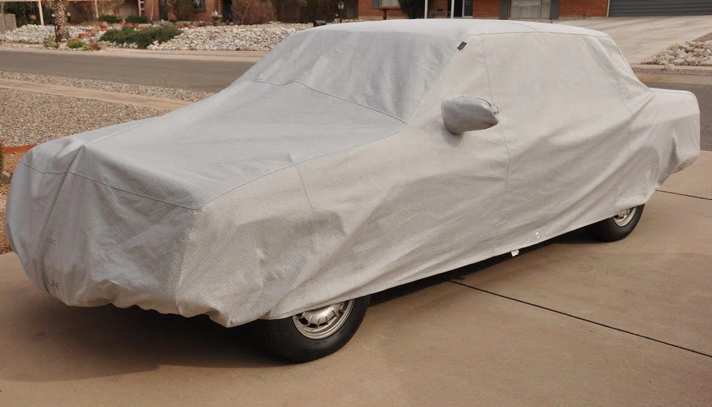 A car parked on a driveway draped with a light beige car cover.